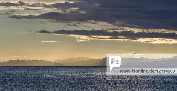 Sonnenstrahlen  die durch die Wolken über den Bergen und dem Meer bei Sonnenaufgang scheinen  Abel Tasman National Park; Neuseeland