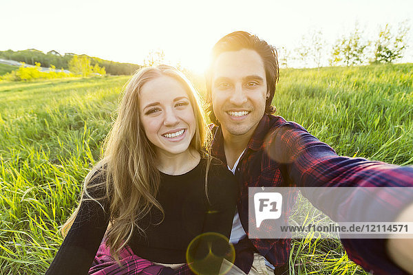 Young couple in a park posing for a self-portrait with their cell phone; Edmonton  Alberta  Canada