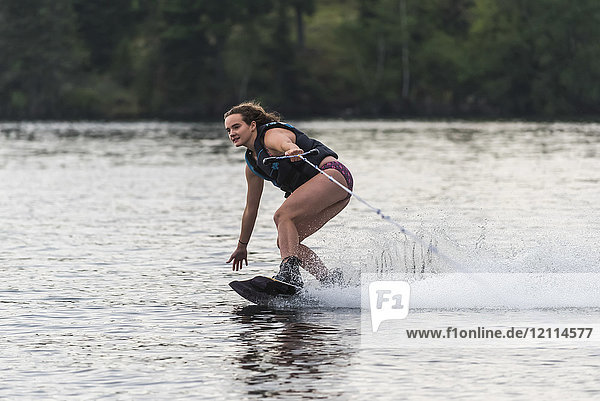 A teenage girl wakeboarding behind a boat on a lake; Lake of the Woods  Ontario  Canada