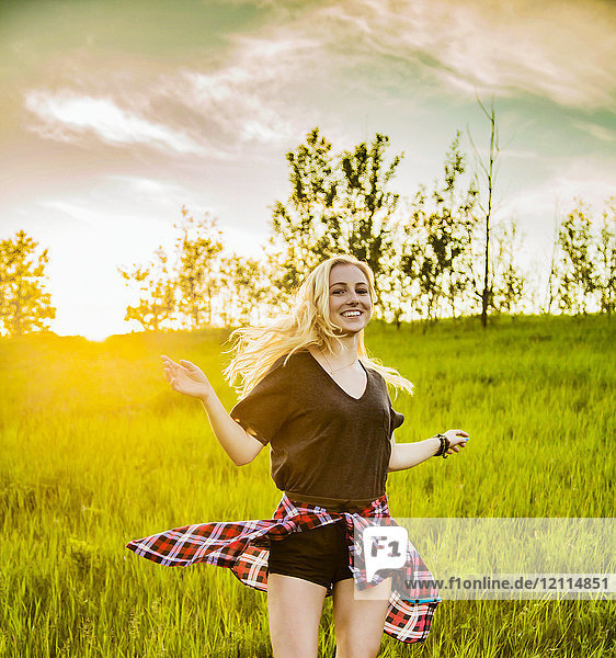 A young woman with long blond hair twirls and runs freely in a grass field in a park; Edmonton  Alberta  Canada