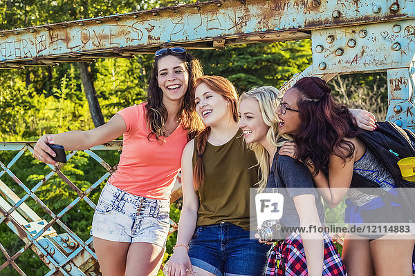 Eine Gruppe von vier Freundinnen posiert für ein Selbstporträt mit einem Smartphone auf einer Brücke in einem Park; Edmonton  Alberta  Kanada