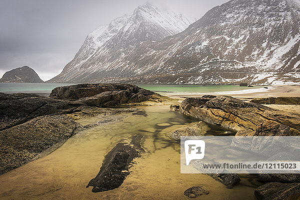 A landscape with rugged mountains and sand along the coastline under a cloudy sky; Nordland  Norway