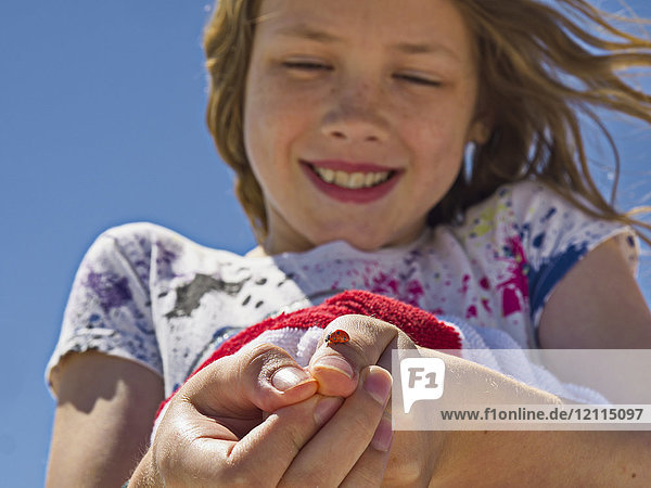 A young girl shows off a ladybug (Coccinellidae) she caught and is holding on her thumb; Destin  Florida  United States of America
