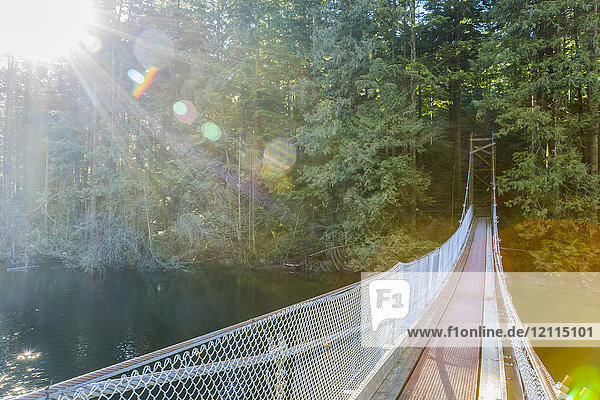 Sonnenschein erhellt den Weg entlang einer Hängebrücke über das Ende des Buntzen Lake Trail  um den Weg in die Waldwege in der Nähe von Vancouver fortzusetzen; British Columbia  Kanada
