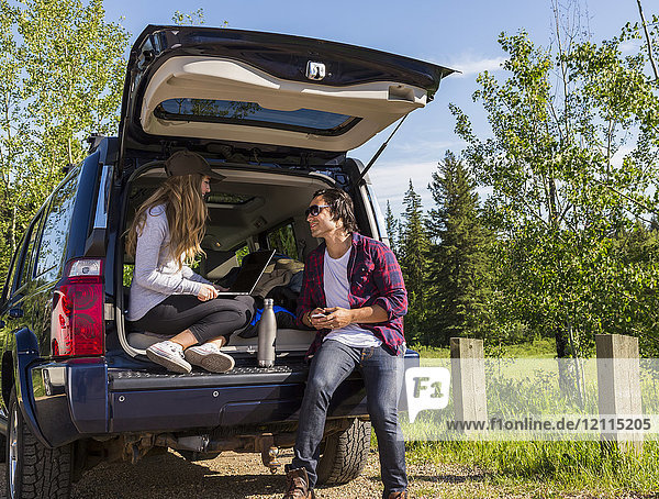 Junges Paar  das in seinem Fahrzeug mit geöffneter Heckklappe auf einen Laptop schaut; Edmonton  Alberta  Kanada