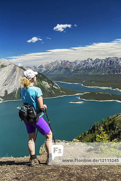 Wanderin auf dem Gipfel eines Bergrückens mit Blick auf einen farbenfrohen Bergsee und eine Bergkette in der Ferne mit blauem Himmel und Wolken; Kananaskis Country  Alberta  Kanada