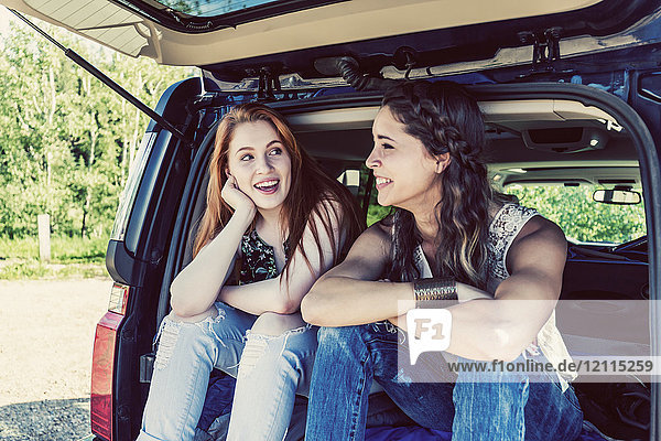 Zwei junge Frauen auf einer Autoreise sitzen auf dem Rücksitz eines Fahrzeugs und reden und lachen miteinander; Edmonton  Alberta  Kanada
