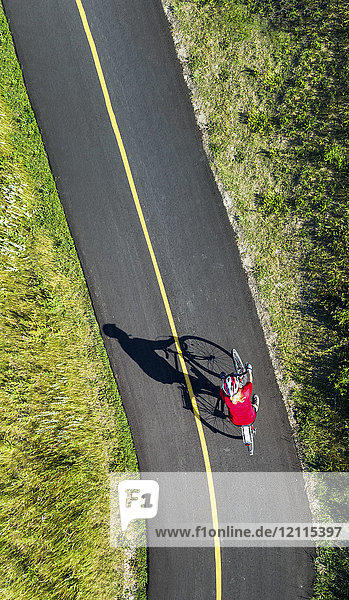 View from directly above a cyclist in a red shirt on a paved cycling trail; Calgary  Alberta  Canada