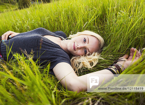 Porträt einer jungen Frau mit langen blonden Haaren  die in einem Park im Gras liegt; Edmonton  Alberta  Kanada