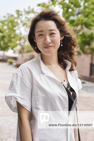 Porträt einer Frau mit langen braunen Haaren in Weiß  die im Freien steht und in die Kamera lächelt.
