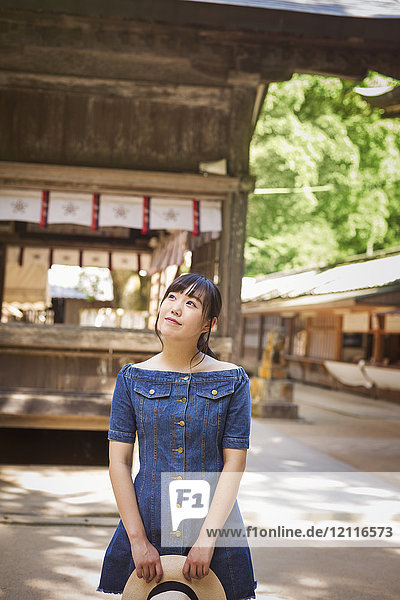 Junge Frau in blauem Kleid und mit Hut in der Hand am Shinto Sakurai-Schrein Fukuoka Japan.