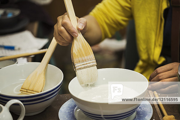 Close up of person working in a Japanese porcelain workshop  glazing white bowls with paintbrush.