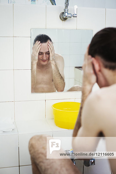 Ein Mann wäscht sein Gesicht in einem Badehaus  Blick in einen Spiegel.