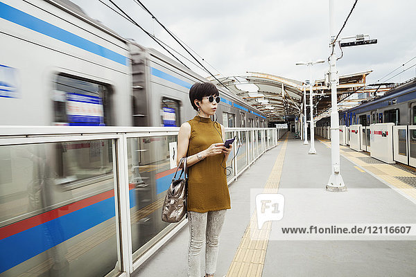 Auf dem Bahnsteig einer U-Bahn-Station stehende Frau mit Sonnenbrille  Tokio-Pendler.