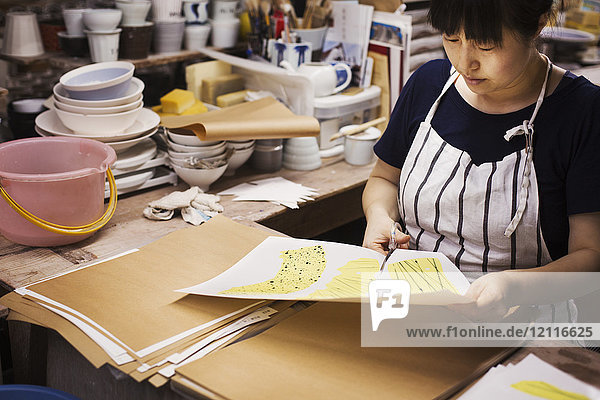 Frau sitzt in einer japanischen Porzellanwerkstatt und schneidet mit einer Schere Muster aus.