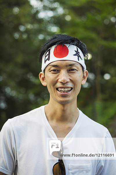 Porträt eines Mannes mit Stirnband und japanischer Flagge  der in die Kamera lächelt.