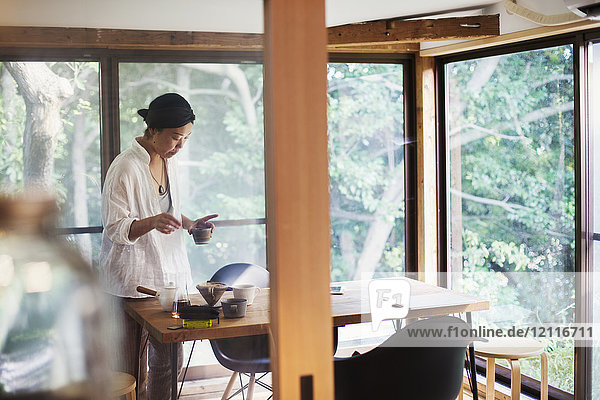 Woman standing indoors by a table holding small bowl.