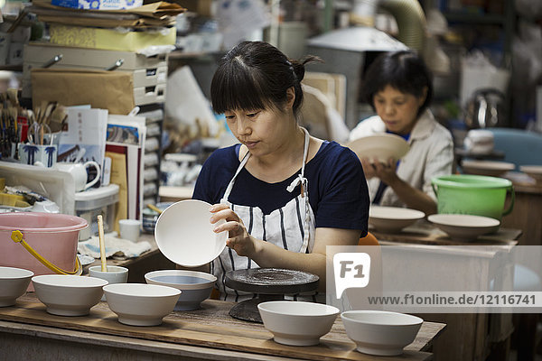 Zwei Frauen sitzen in einer Werkstatt und arbeiten an japanischen Porzellanschüsseln.