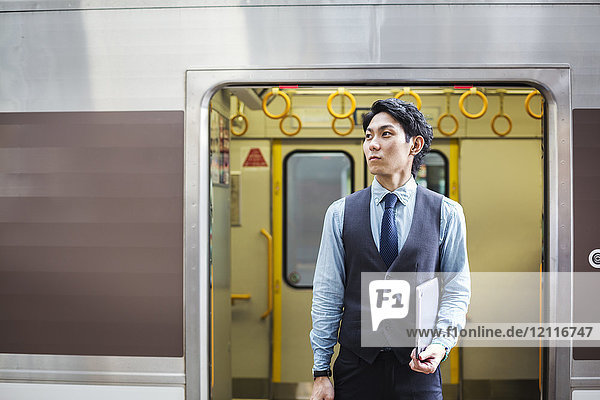 Geschäftsmann in blauem Hemd und Weste auf dem Bahnsteig des Bahnhofs stehend  Laptop in der Hand.