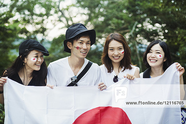 Lächelnder Mann und drei junge Frauen stehen im Freien  Gesichter bemalt  japanische Flagge haltend.