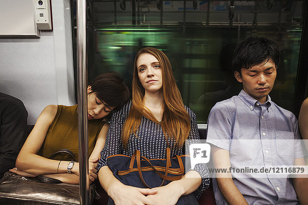 Drei Personen  zwei Frauen und ein Mann  die nebeneinander in einem U-Bahn-Zug sitzen  Pendler aus Tokio.