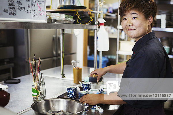 Waitress working in the kitchen of a Japanese sushi restaurant  smiling at camera.