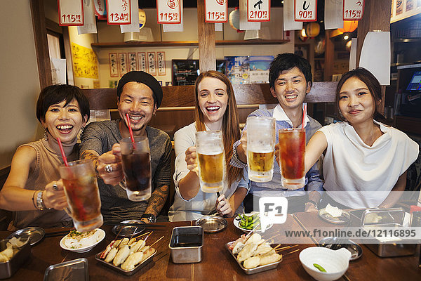 Fünf Personen sitzen nebeneinander an einem Tisch in einem Restaurant und halten große Gläser mit Erfrischungsgetränken und Bier in der Hand.