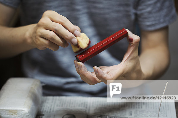 Nahaufnahme einer Frau  die in einer japanischen Porzellanwerkstatt arbeitet  mit rotem Farbstab und Schwamm in der Hand.