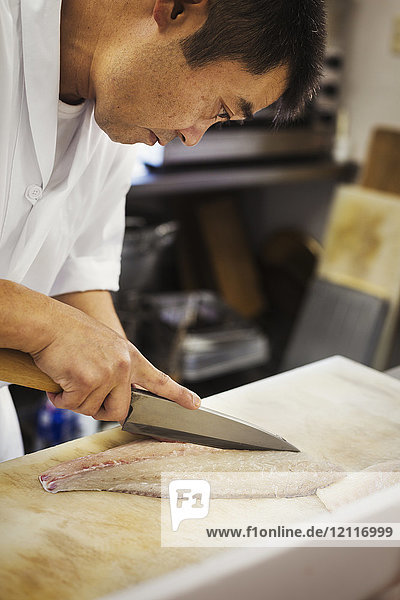 Chefkoch  der an der Theke eines japanischen Sushi-Restaurants arbeitet und Fischfilet in Scheiben schneidet.