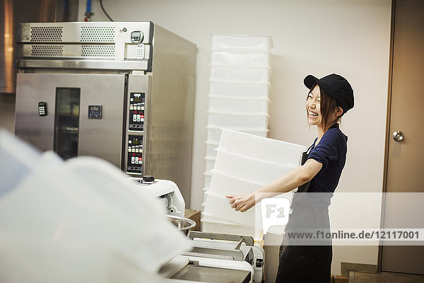 Frau arbeitet in einer Bäckerei  trägt eine Baseballmütze und trägt einen Stapel weißer Plastikkisten.