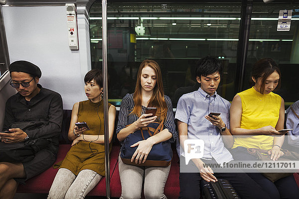 Fünf Menschen sitzen nebeneinander in einem U-Bahn-Zug  Tokio-Pendler.