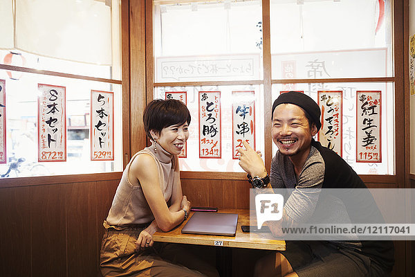 Zwei Menschen  ein lächelnder Mann und eine lächelnde Frau  sitzen an einem kleinen Tisch in einem Cafe.
