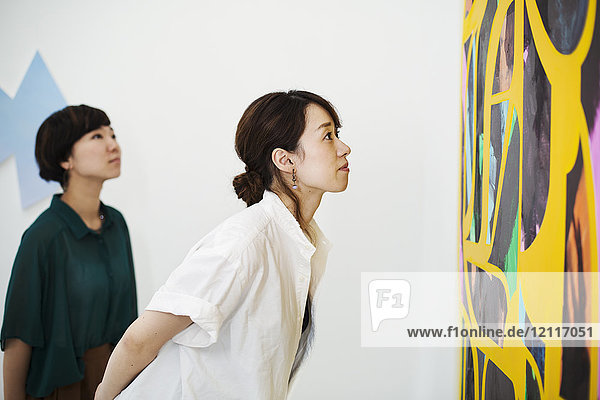 Zwei Frauen stehen in einer Kunstgalerie und betrachten ein abstraktes modernes Gemälde.