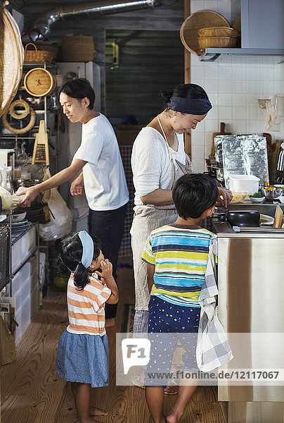 Mann  Frau mit Schürze  Junge und junges Mädchen stehen in einer Küche und bereiten Essen vor.