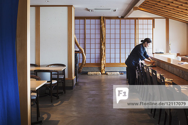 Kellnerin  die an einem Tresen in einem japanischen Sushi-Restaurant steht und Gedecke vorbereitet.