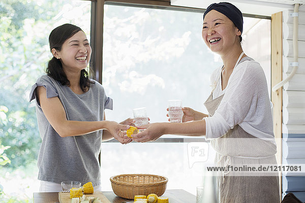 Zwei lächelnde Frauen  die drinnen an einem Tisch stehen und Trinkgläser halten.