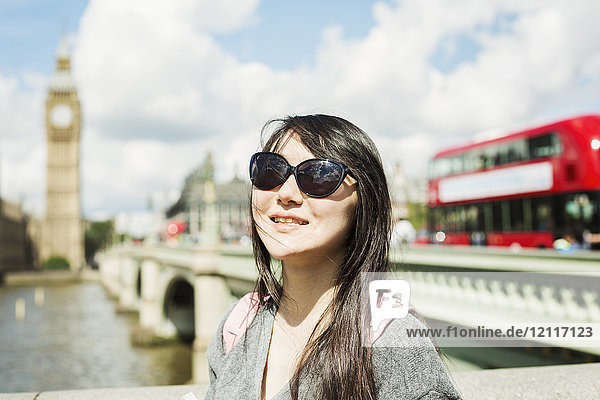 Lächelnde Frau mit schwarzen Haaren und Sonnenbrille auf der Westminster Bridge über die Themse  London  mit dem Houses of Parliament und Big Ben im Hintergrund.