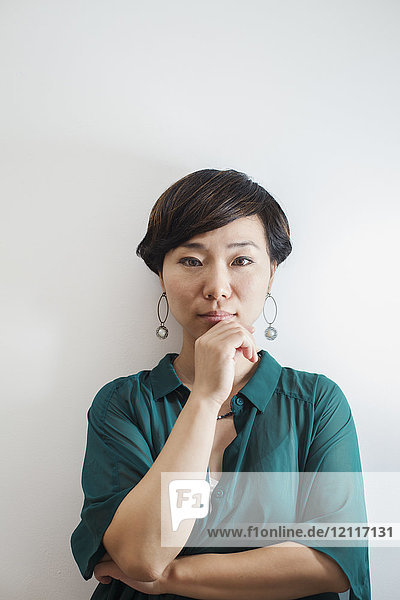 Woman with short black hair wearing green shirt standing in art gallery  hand on chin  looking at camera.