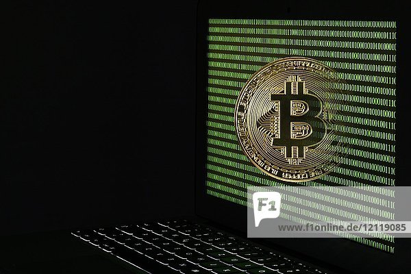 Symbolbild Kryptowährung  digitale Währung  goldene physische Münze bitcoin Laptop mit digitalem Binärcode