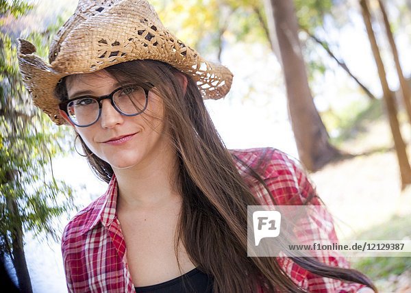A casual portrait of a 26 year old woman with long brown hair and big glasses  on a country road.