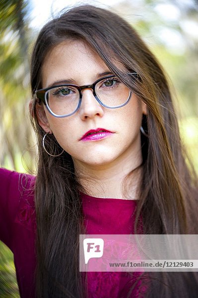 A casual portrait of a 26 year old woman with long brown hair and big glasses  outdoors.