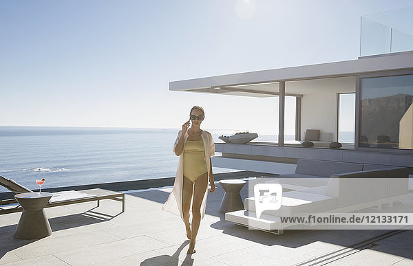 Frau im Badeanzug  die auf einer sonnigen  modernen  luxuriösen Musterhaus-Terrasse mit Meerblick spazieren geht