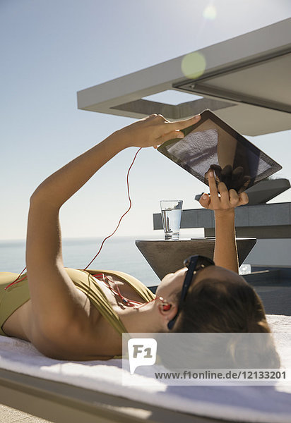 Frau beim Sonnenbaden,  mit digitalem Tablet auf Liegestuhl auf sonniger Terrasse