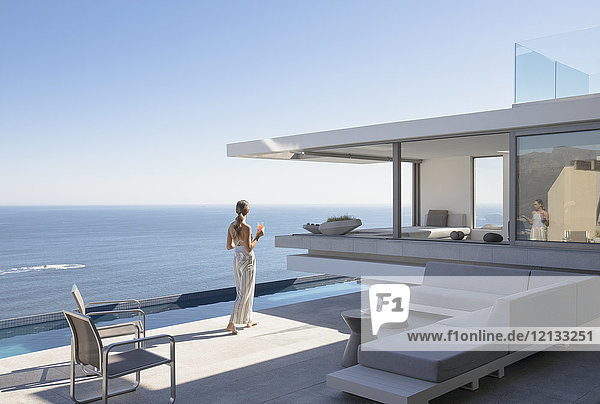 Frau auf sonnigem  modernem  luxuriösem Haus mit Außenterrasse und Meerblick