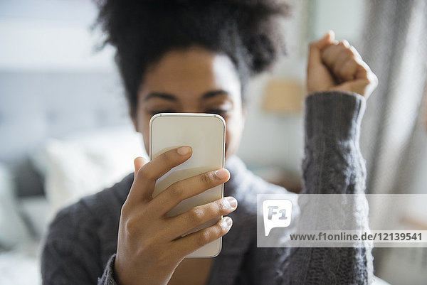 Afroamerikanische Frau feiert  während sie eine SMS auf ihrem Handy schreibt