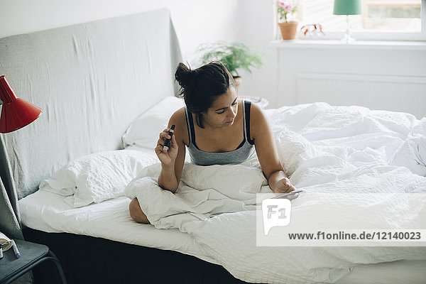 Frau bei der Blutuntersuchung mit dem Handy im Bett im Schlafzimmer