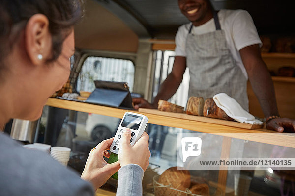 Mid adult woman using credit card reader to pay salesman at food truck
