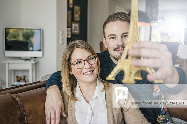 Smiling couple sitting on couch at home holding Eiffel tower model