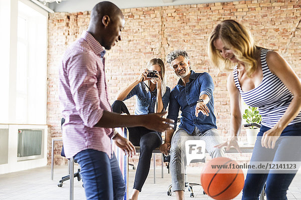 Frau fotografiert Kollegen beim Basketballspielen im Büro