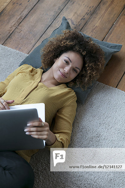 Smiling young woman lying on the floor at home with laptop